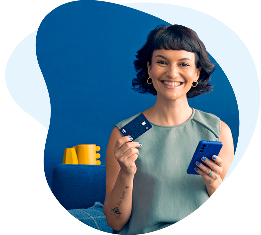 Una mujer joven de pelo negro corto y flequillo segurando la tarjeta de débito de Mercado Pago en la mano derecha, y un celular en la izquierda.