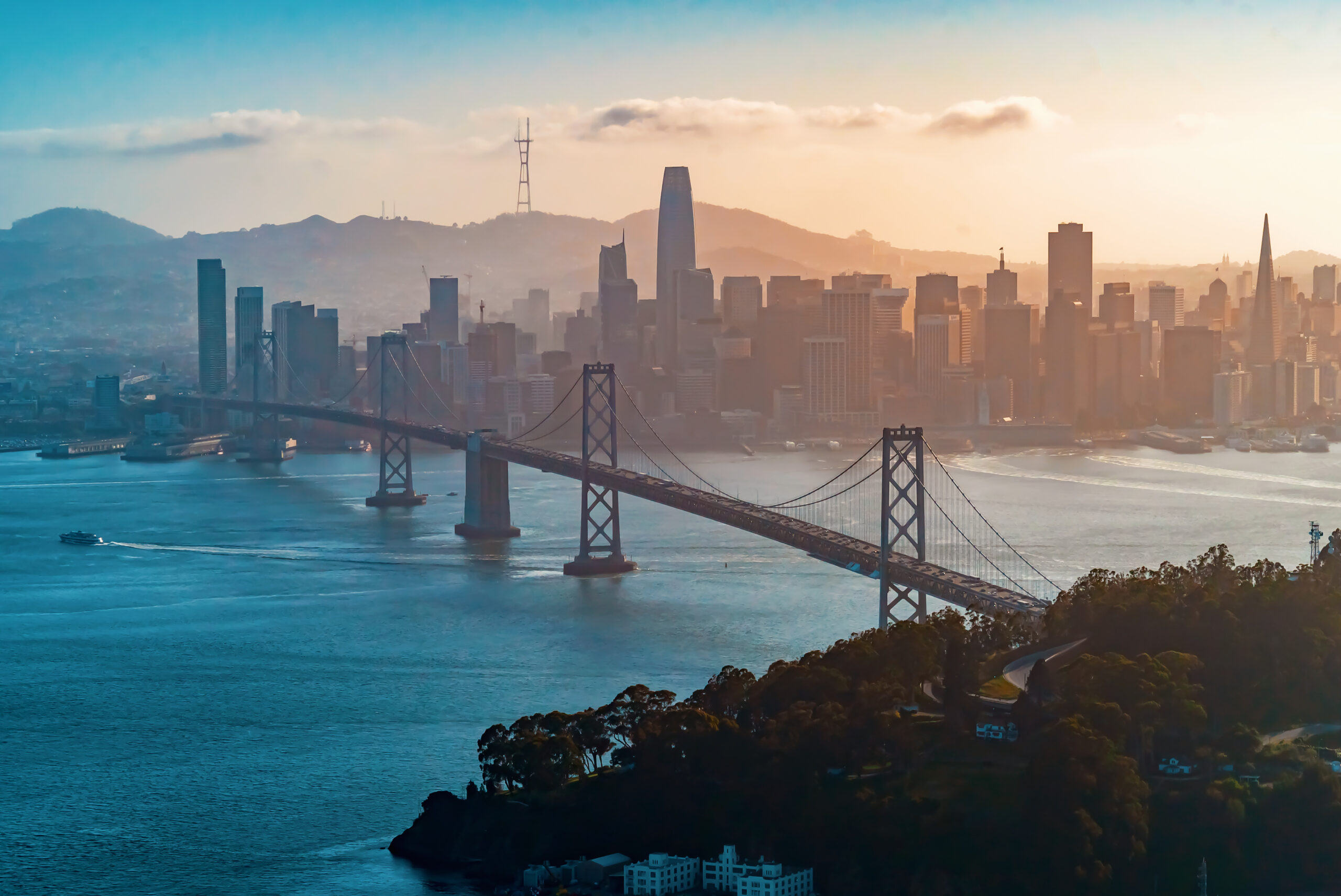 A bridge over a body of water leads to a city at sunset or sunrise.