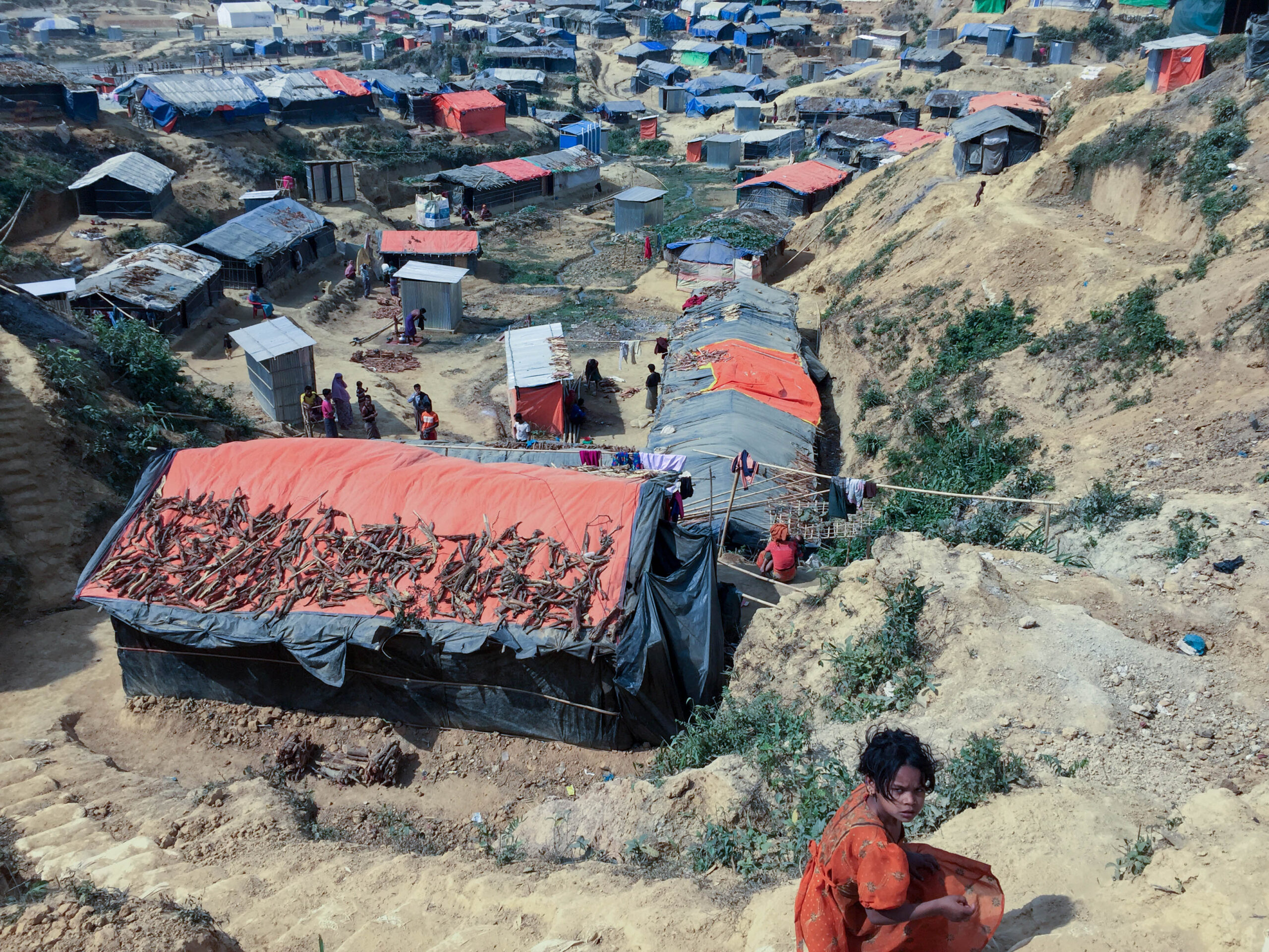 A girl with brown hair wearing a red dress sits outside above several structures.