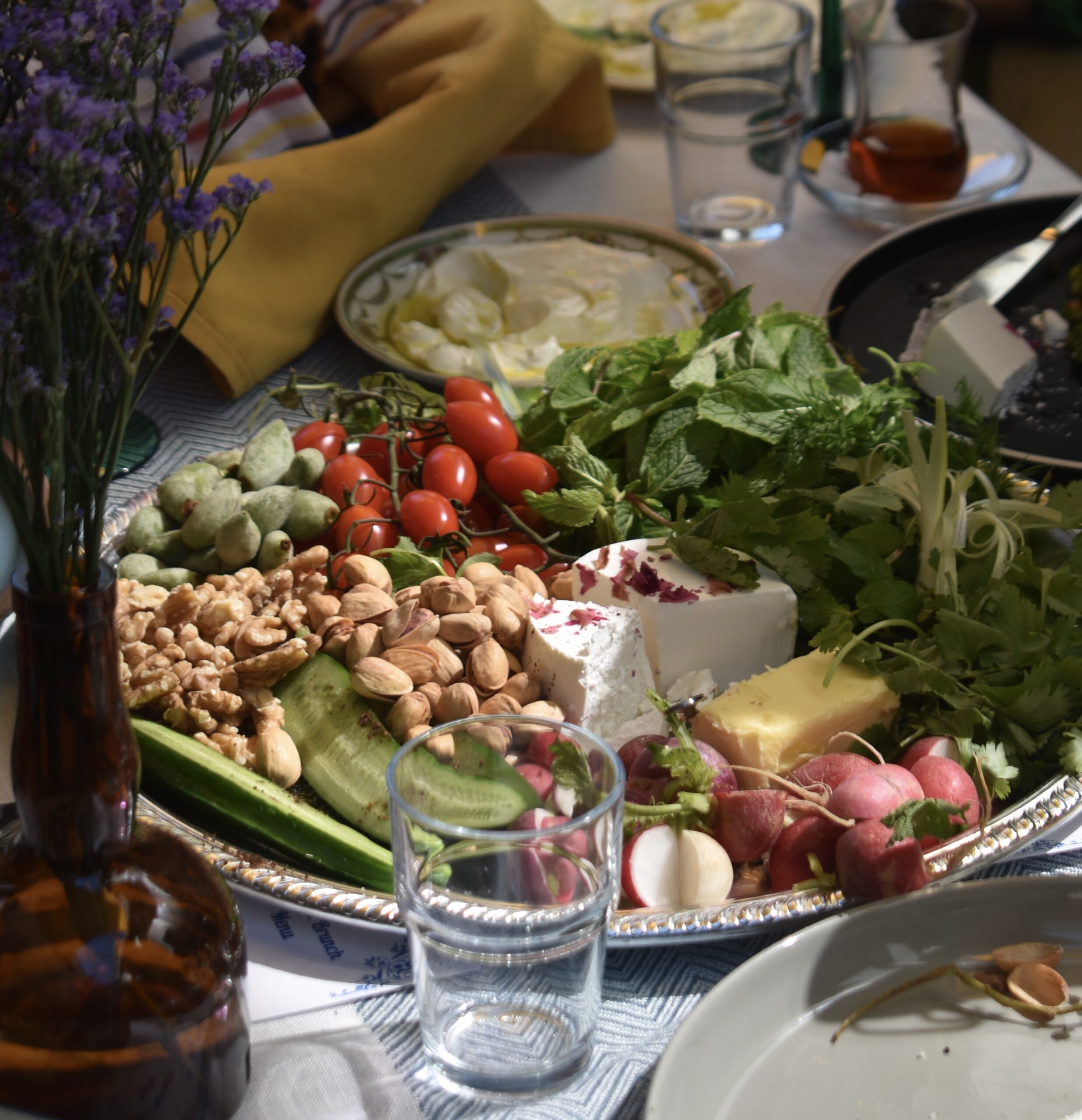 A platter with mint, herbs, nuts, tomatoes, and olives.