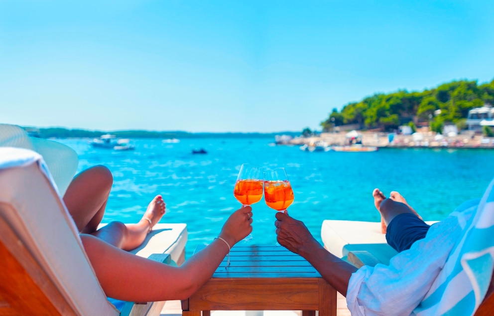 PHOTO: Couple relaxing and toasting with a Spritz cocktail on a beach deck over the ocean.