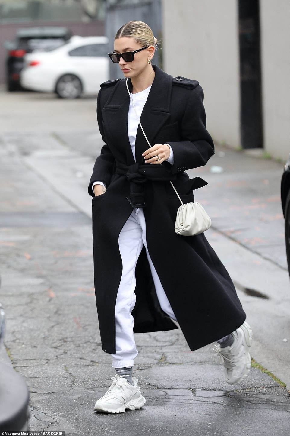 Making moves: Hailey donned a long black robe coat over white sweats and white Balenciaga track sneakers which retail for $955