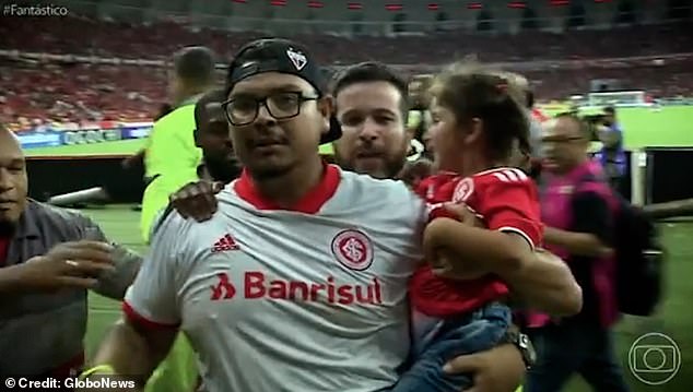 Pictured: The football fan is seen being dragged off the pitch by stewards while carrying a young girl in his arms, after kicking a player between the legs