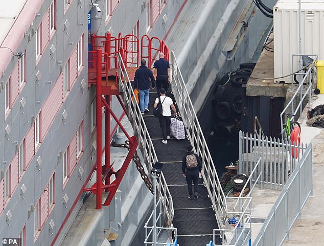 People are seen carrying rucksacks and plastic bags as they climb aboard the Bibby Stockholm today