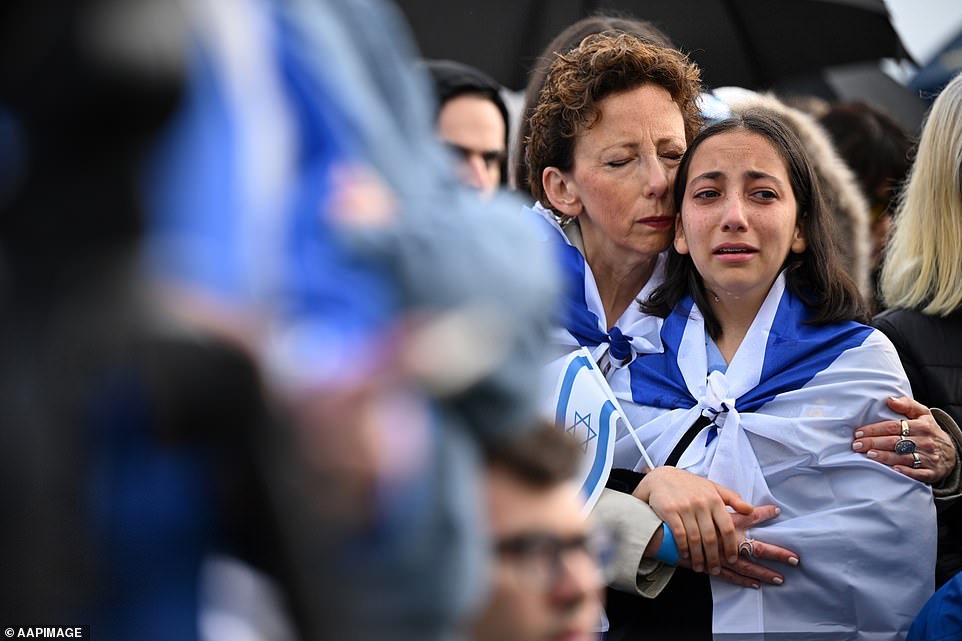 AUSTRALIA: An emotional teenager is comforted during a vigil for the victims of the recent attacks in Israel, at Caulfield Park in Melbourne on Friday