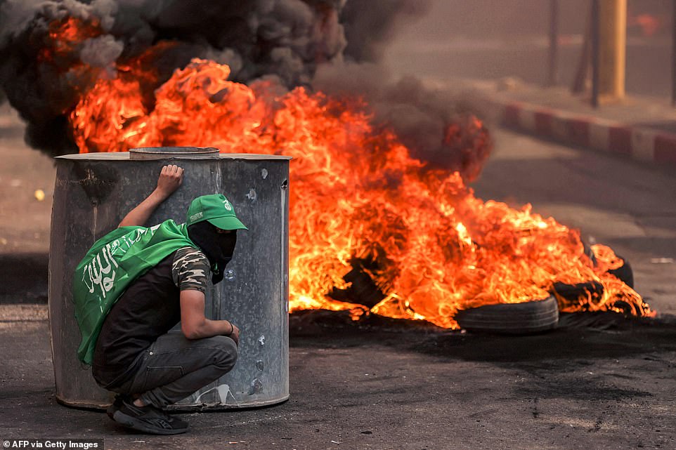 WEST BANK: A masked Palestinian protester takes cover near flaming tires during clashes with Israeli forces following a rally in solidarity with Gaza by supporters of the Fatah and Hamas movements, in the city of Hebron in the occupied West Bank on Friday