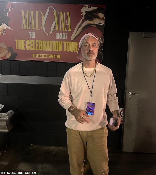 Dapper: Taika meanwhile looked casual in a long white T-shirt and beige trousers as he posed in front of the Celebration Tour sign