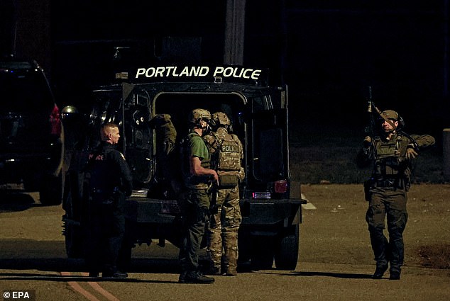 Police officers surround an armored law enforcement vehicle parked on the parking lot of the Lisbon High School gymnasium