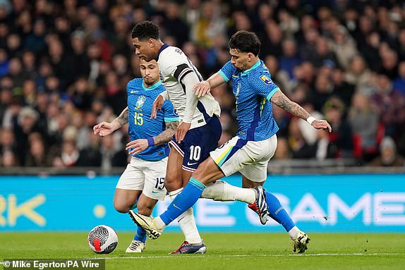 England's Jude Bellingham (centre) is tackled by Brazil's Lucas Paqueta (right) during the international friendly match at Wembley Stadium, London. Picture date: Saturday March 23, 2024. PA Photo. See PA story SOCCER England. Photo credit should read: Mike Egerton/PA Wire.RESTRICTIONS: Editorial use only. Commercial use only with prior written consent of the FA. No editing except cropping.