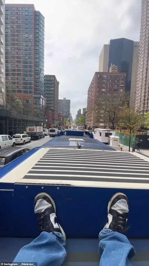 A man wearing Nike shoes can be seen sitting on the roof of an M15 articulated bus as the vehicle barrels down Second Avenue in Manhattan's Murray Hill neighborhood