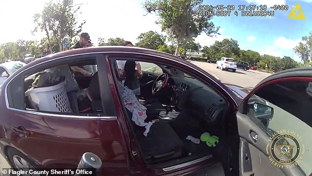 The two adults that were found standing outside of the car when officers arrived said that the child was inside the Nissan Altima for 10 minutes. (pictured: the little girl being taken out of the driver's seat)