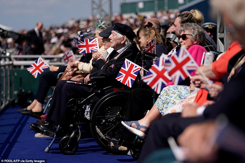 Veterans holding Union flags sit in the front row of today's national D-Day commemoration