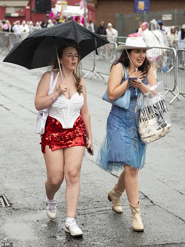 One fan holds an umbrella while another looks less than pleased as they battle the weather