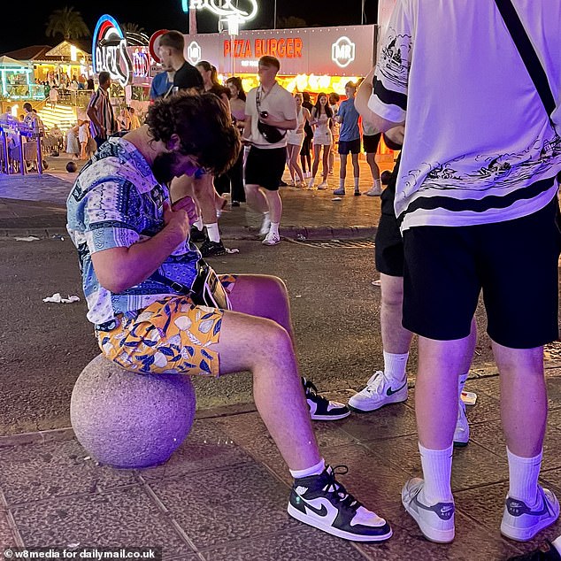 A holidaymaker sits outside on the Magaluf strip after a night out with friends on Sunday