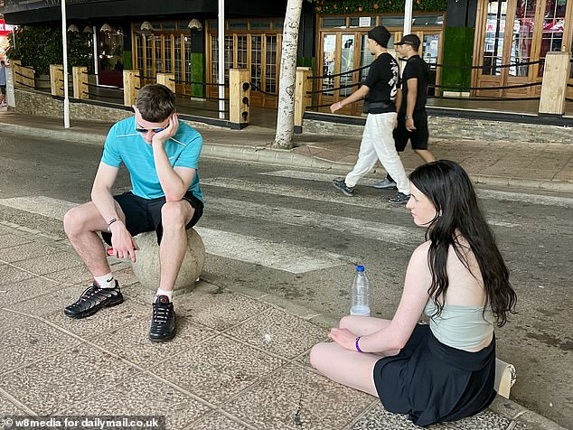 Tired holidaymakers are seen resting on the pavement after a night out on the Magaluf strip