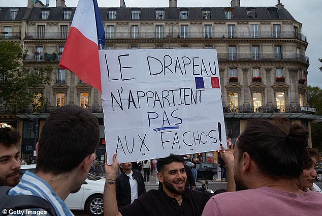 A man holds a board reading the French flag doesn't belong to fascists as tens of thousands people gather in Paris to protest against the far-right