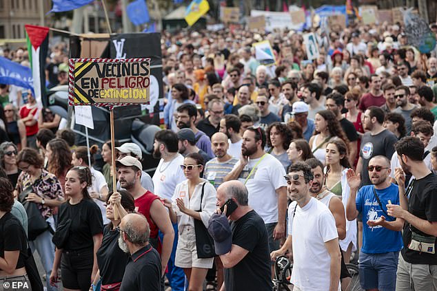 A woman carries a sign that reads 'neighbours in danger of extinction' through Barcelona