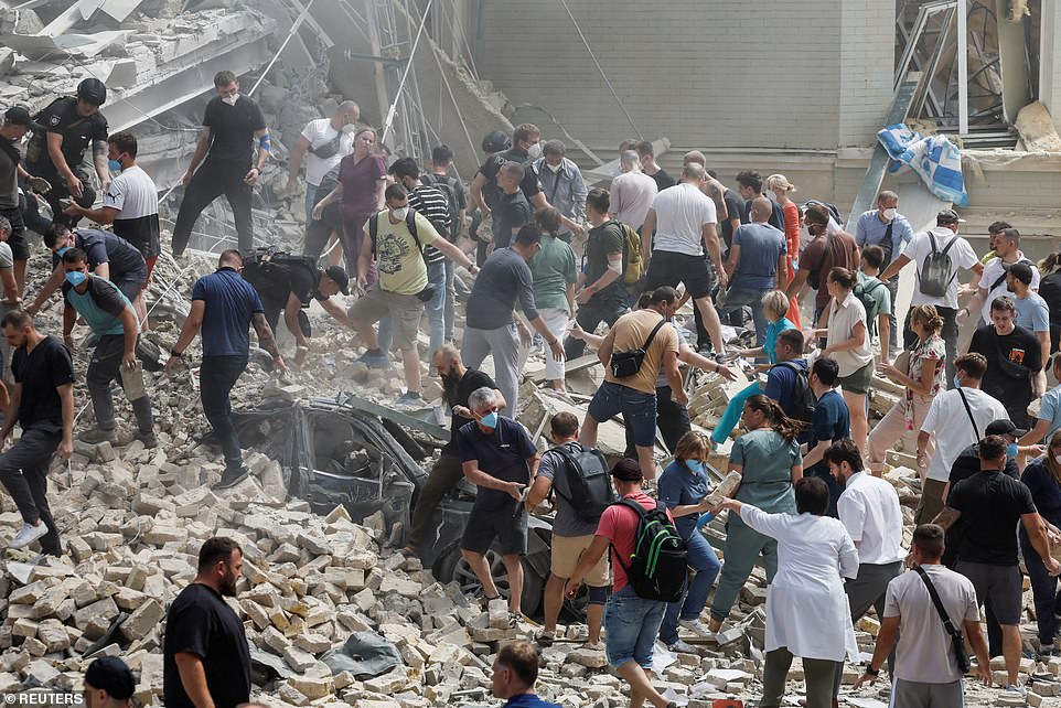 Ukrainian President Volodymyr Zelensky said Russia had targeted five cities with more than 40 missiles of different types in a 'genocidal' attack, adding that people were trapped under the rubble of the children's hospital. Pictured: People help to clear the rubble at the site