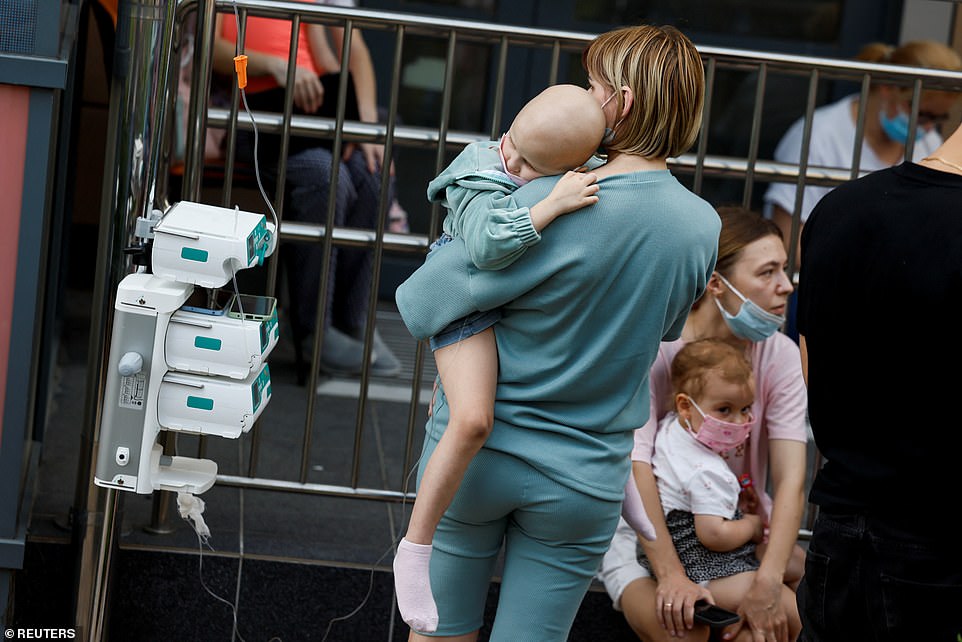 A woman carries a child near Ohmatdyt Children's Hospital after it was struck by missiles