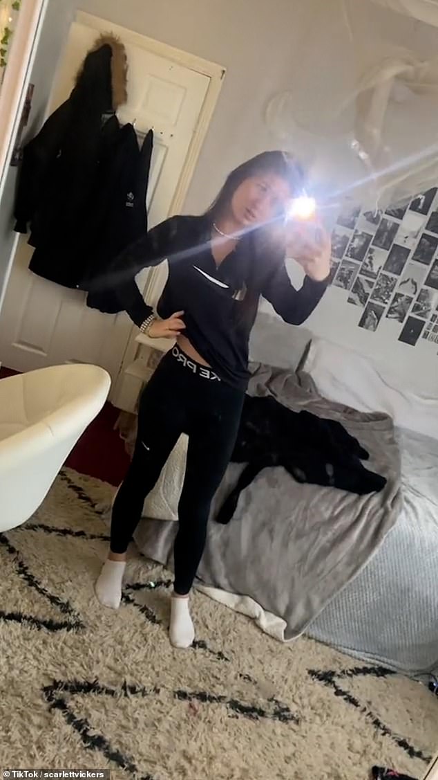 Scarlett places her hand on her hip as she poses wearing a black top and jogging bottoms in her bedroom