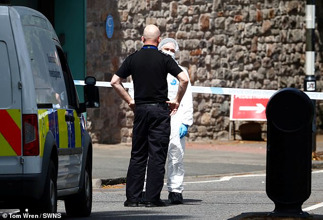 A uniformed police officer speaks with a member of the forensics team at the scene today