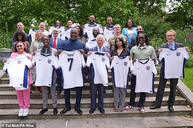 The King held an England shirt as he and Idris posed with youth organisers - to show their support for the national team