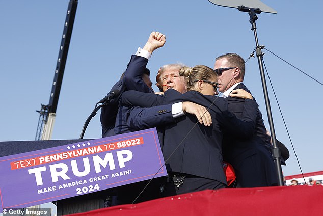 Donald Trump got to his feet and gave a clenched fist salute to his supporters in the crowd before being whisked away by his Secret Service detail