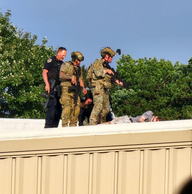 Law enforcement stand over the body of the shooter on a building across from the rally site