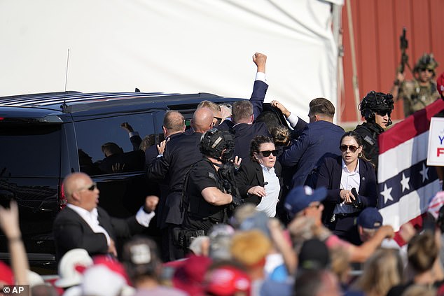 At 6:14pm, Trump raised his fist to the air as he was whisked into his motorcade by his Secret Service agents forming a human shield around him