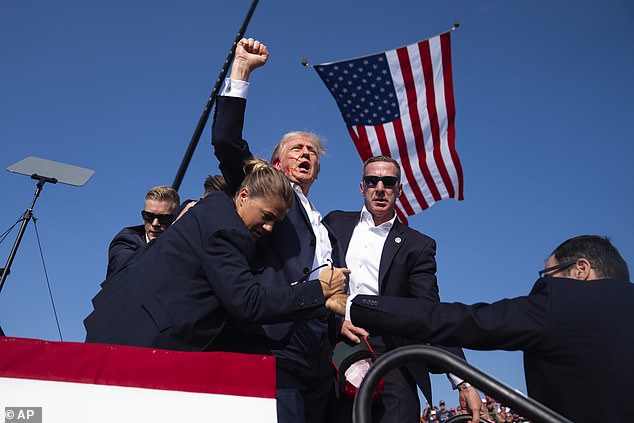 Trump raises a fist to the crowd as he is bundled off stage by security after being shot