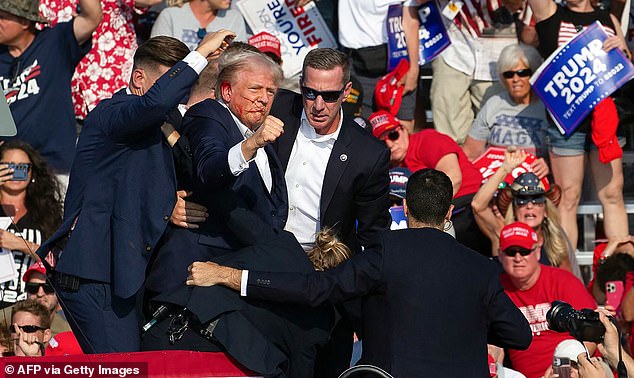 Trump is seen with blood on his face surrounded by secret service agents as he is taken off the stage