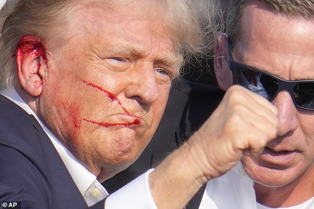 Republican presidential candidate former President Donald Trump gestures while surrounded by U.S. Secret Service agents as he is helped off the stage at a campaign rally in Butler, Pa., Saturday, July 13, 2024