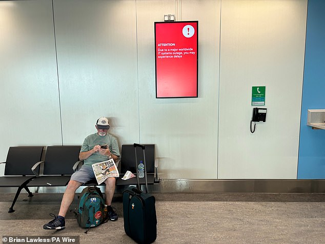 A passenger sits under an information screen in the South Terminal at Gatwick Airport