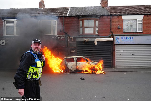 The trio were involved in violent disorder in Middlesbrough on August 4 (pictured: a police officer uses his radio as a car burns behind him)