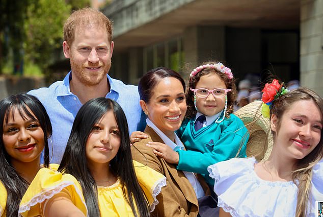 Meghan holds a child as she and Harry pose for photos with students outside the school