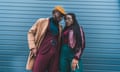 Fashionable couple in jacket and overcoat posing together outside; he has short hair, hers is long and braided