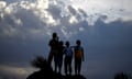 Four boys stand on a hill silhouetted against a dark sky