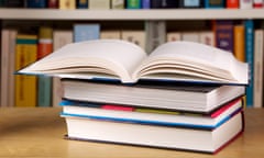 Open book on top of a pile of books. In the background a library shelf