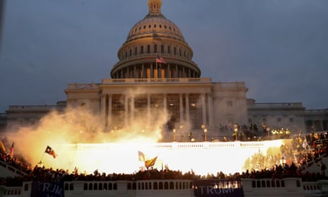 Evening photo of front of columned building with multistory cupola, with a bright light illuminating smoke and US flags.
