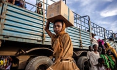 Girl carrying box on her head next to an open-topped truck.