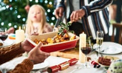 Family Christmas meal with home cooked food being served at dining table, traditional holly with berries garnishing roasted vegetables, Christmas cracker on table with wine and candles