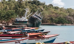 Two large vessels sit at an angle with their hulls out of the water behind a group of small wooden fishing boats