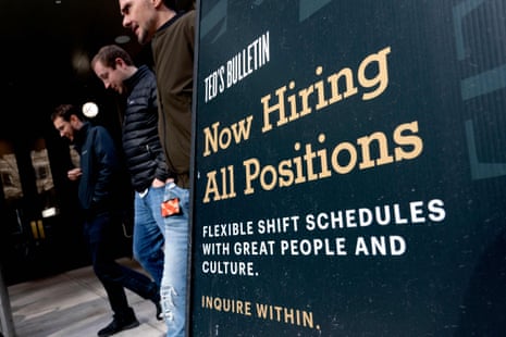 People walk past a now-hiring sign