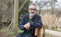 David Baddiel sitting on bench among trees.