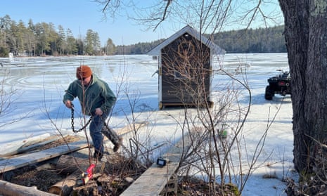 man holds chain as he walks onto shore away from small house on ice