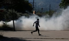 A man runs for cover as riot police launch tear gas in an effort to remove street vendors in the Champs de Mars area, next to the National Palace, in Port-au-Prince, Haiti, Tuesday, April 2, 2024. (AP Photo/Odelyn Joseph)