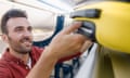 Portrait of cheerful man pulling out suitcase from hand luggage compartment, overhead locker while traveling by plane<br>2GF1YM6 Portrait of cheerful man pulling out suitcase from hand luggage compartment, overhead locker while traveling by plane