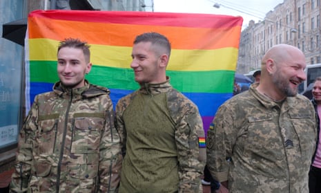 Three Ukrainian soldiers smiling in front of a rainbow flag at the pride march in Kyiv.