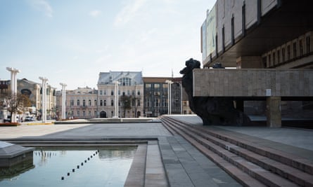 side-on view of the Kharkiv opera house with steps and water feature in front and older buildings ahead across the paved square