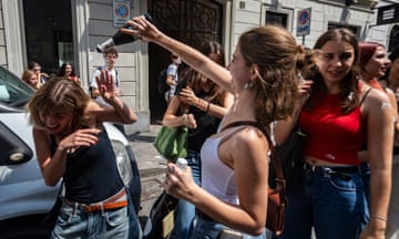 A girl pours a drink over her friend who laughs during end of term celebrations